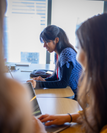 Three women work on laptops at a large table.