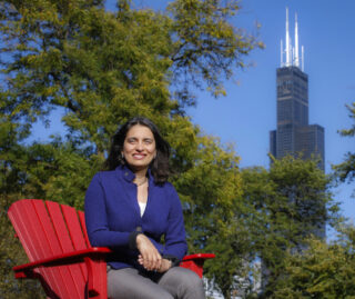 Amita Shetty on UIC's campus in a large red Adirondack chair, with the Sears Tower in the background