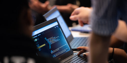 Students in a Break Through Tech program code on laptops as a mentor looks on