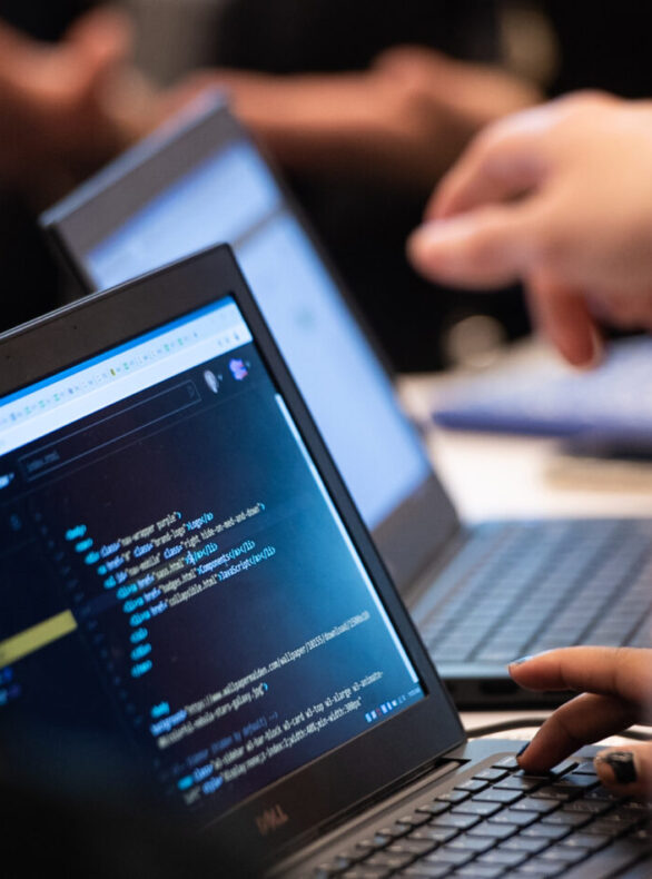 Students in a Break Through Tech program code on laptops as a mentor looks on