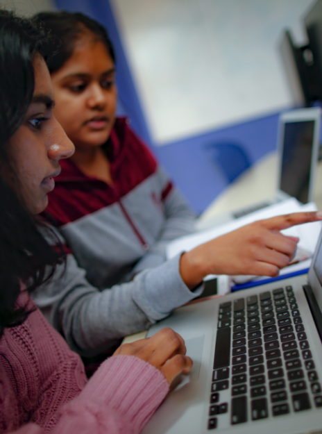 One student points at information on a computer screen to get an opinion from a classmate