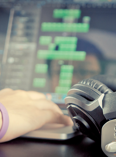 Close-up of a girl editing audio on a laptop with headphones nearby