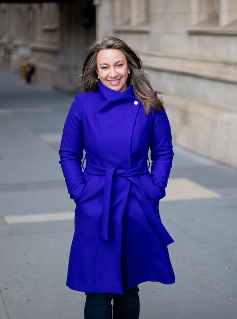 Reem Jaghlit, head of diversity, equity, and inclusion for ActiveCampaign, wears a bright blue coat on the sidewalk in front of a building.