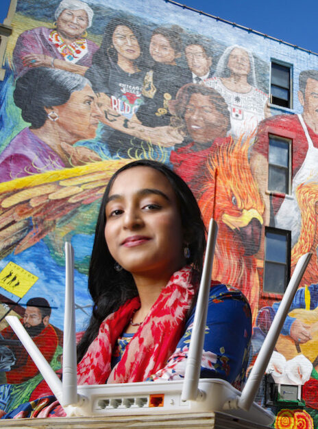 UIC student Afifa Nadeem poses with networking technology in front of a mural by Pablo Serrano in the Chicago neighborhood of Pilsen