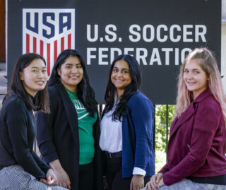 Four of the five 2021 U.S. Soccer Sprinterns pose in front of a U.S. Soccer Federation banner