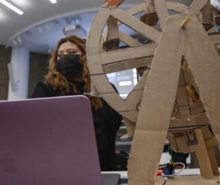 a CS 111 student with their programmable Rube Goldberg element, which resembles a water wheel built from cardboard