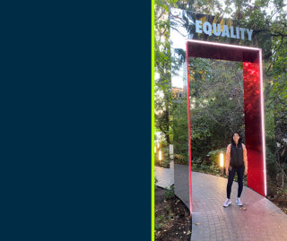 Lydia Tse stands on a pathway underneath a rectangular mirrored arch with the word 