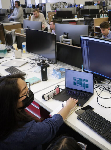 A Break Through Tech Chicago Sprintern works at a laptop connected to larger monitor displays at the financial services firm PEAK6