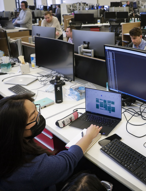 A Break Through Tech Chicago Sprintern works at a laptop connected to larger monitor displays at the financial services firm PEAK6