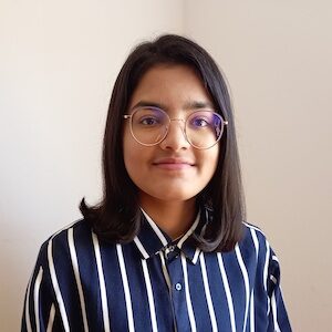 headshot of Nandini Jirobe in a blue and white striped shirt against a cream-colored background