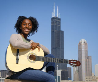 Musically inclined UIC computer science student Charlotte Andry poses with her guitar, with the Sears Tower in the background
