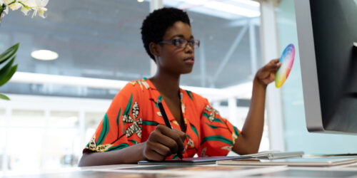 a Black female graphic designer uses a color wheel to assess the design on her panel monitor