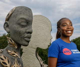 Tomi Okunola, wearing a blue UIC computer science t-shirt, poses in front of a sculpture of an African woman in Chicago